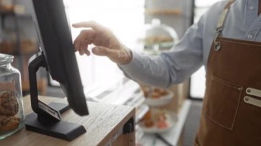 Pastanede dokunmatik ekran kullanan bir adam, eller kasiyer sistemini işaret ediyor tezgahta kurabiye kavanozu, kapalı mekanda
