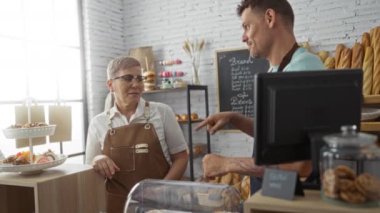 Kadın ve erkek, çeşitli hamur işleriyle dolu kapalı bir pastanede fırıncı olarak çalışıyor.