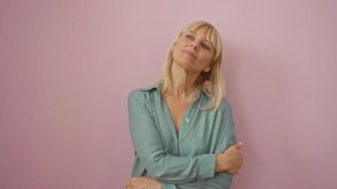 Orta yaşlı, sarışın, tişörtlü, yandan gülümseyen, kendinden emin, güler yüzlü, soyutlanmış pembe arka planda doğal, zarif ve mutlu bir kadın.