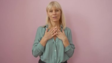 Sağlığına minnettar bir kadın, orta yaşlı, tişört giyen, elleri göğsünde mutlu bir şekilde duran, izole pembe arka planda gülümseyen bir kadın.