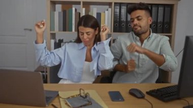 Kadın ve erkek, modern bir ofiste arka planda bilgisayar ve kitap raflarıyla birlikte neşeyle dans ediyor, eğlenceli bir iş ortamını ön plana çıkarıyor.