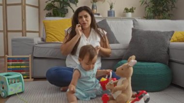Oyuncak ve bitkilerle dolu rahat bir oturma odasında, yerde oturan bebekle telefonda konuşan hayal kırıklığına uğramış bir kadın.