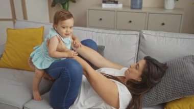 Anne küçük kızıyla rahat bir oturma odasında oynuyor, aile sevgisini ve neşesini içeride gösteriyor.