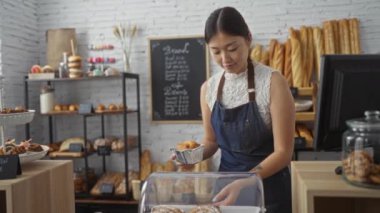 Bir pastanede çalışan güzel bir kadın tezgahta gülümserken ekmek ve hamur işleri düzenliyor.