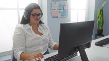 Ofiste kulaklık takan, gülümseyen ve müzikten zevk alan bir kadın.