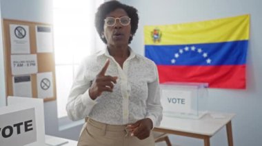 Venezuela seçim koleji odasında oy kullanma materyalleri ve ulusal bayrağıyla konuşan siyahi bir kadın..