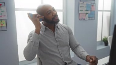 Genç adam masada oturmuş bilgisayar ekranına bakarken telefonda konuşuyor.