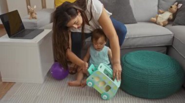 Anne, arka planda oyuncak ve dizüstü bilgisayarla küçük kızıyla oturma odasında oynuyor.