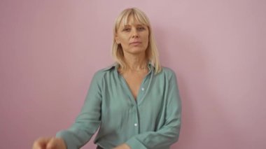 Depresyon ve can sıkıntısı, orta yaşlı kadın, sarışın, gömlekli, çapraz kollu, soyutlanmış pembe arka planda yorgun görünüyor.