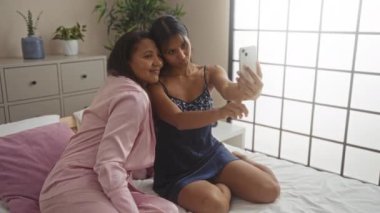 Anne ve kızı yatak odasında oturup selfie çekiyorlar. Evde sevgi ve aile bağlarını gösteriyorlar.