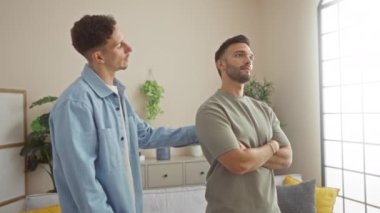 Modern bir oturma odasında iki adam duygusal bir uzlaşma içindeler. Büyük pencerelerden içeri ışık saçan samimi bir evde sevgi ve destek gösteriyorlar..