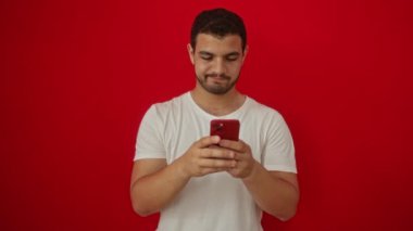 Genç İspanyol erkekten, öfkeli reddedilme ve izole edilmiş kırmızı arka planda akıllı telefondan hoşlanmayan hareketler.