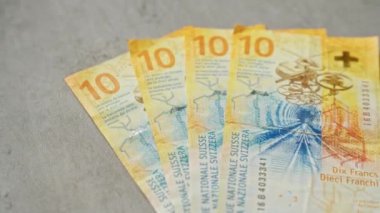 İsviçre banknotları, özellikle on frank banknotlar, canlı renkler ve İsviçre ekonomisini sembolize eden karmaşık tasarımlar içeren beton bir yüzey üzerinde düzenlenmiştir.