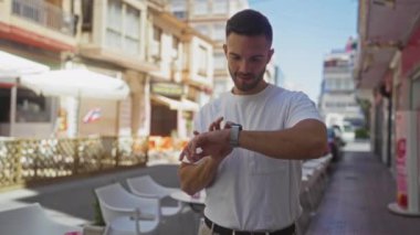 Sakallı, genç İspanyol bir adam güneşli bir günde şehir sokağında dikilip akıllı bakışlarını kontrol ediyor..