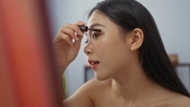 Genç Asyalı bir kadın güzellik salonuna maskara sürüyor. Huzurlu bir sağlık merkezinde kendine bakım anı yakalıyor.