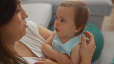 Bebekleri kucağında tutan, şefkatli ve sevgi dolu bir kadın. Aile bağlarını ve anneliğini sıcak bir oturma odasında gösteriyor.