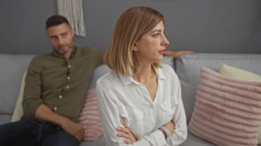 Oturma odasındaki bir kanepede oturan erkek ve kadın kollarını kavuşturup gergin bir şekilde içerideki gerginliği yansıtıyorlar.