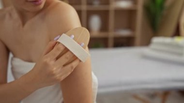 Kaplıcada omzunu tahta bir fırçayla ovalayan bir kadın huzur merkezinde, beyaz bir havlu giyiyor, cilt bakımı, rahatlama ve güzellik sergiliyor.