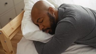 Genç adam bir yatak odasında kapalı bir yatakta uyuyor, gri bir gömlek giyiyor, huzurlu bir yüz ifadesi var.