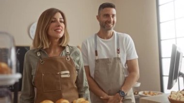 Önlük giyen kadın ve erkek pastanenin iç kısmında birlikte çalışıyorlar.