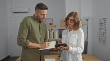 İş adamı ve iş kadını modern ofis ortamında tablet ve defterle çalışmayı tartışıyor