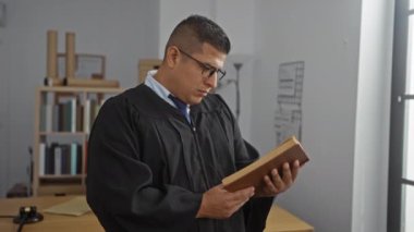 Ofisteki İspanyol adam yargıç cübbesi giyip iç mekanda kitap okuyor.