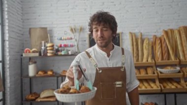 Fırında çalışan yakışıklı genç adam fırında yeni pişmiş yiyecekler sergiliyor. Kapalı bir dükkanda sergileniyor.
