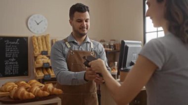 Pastanede çalışan adam, cep telefonu mağazası dekorasyonunu ve tezgahta lezzetli hamur işlerini kullanarak kadınlardan para alıyor.
