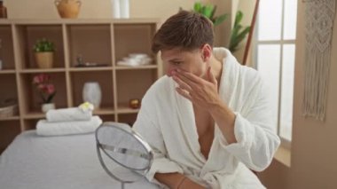 Beyaz cüppeli bir adam aynaya bakarken yüz kremi sürüyor.