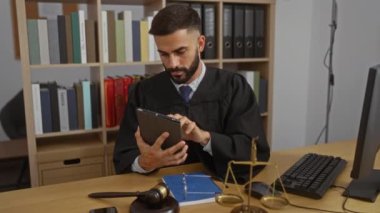 İspanyol bir adam, avukat, ofiste kitap rafları, pulları, tokmağı ve masası olan bir tablet kullanıyor.