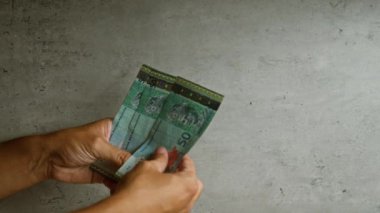 Malezya halkasını somut bir zemine dayandıran adam, banknotların detaylarını vurguluyor ve mali işlem veya ödeme bağlamını öneriyor.