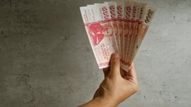 Beton zemine karşı el ele tutuşan İzlanda Krona tarafsız bir ortamda parmaklarını ve parasını gösteriyor..