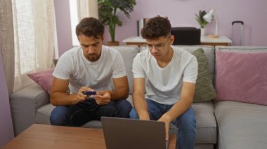 Baba ve oğul rahat bir oturma odasında dizüstü bilgisayar ve kredi kartı kullanarak aile, aşk ve teknolojiyi bir ev ortamında ön plana çıkarıyorlar..