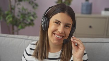 Modern bir oturma odasında mikrofonlu, kulaklık takan gülümseyen bir kadın..