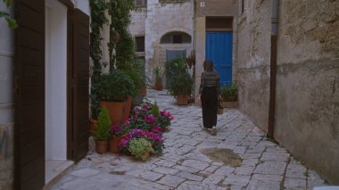 Genç İspanyol bir kadın polignano 'da kaldırım taşı caddesinde yürüyor. Bir kısrak, puglia, İtalya, renkli çiçekler ve kırsal binalarla süslenmiş..