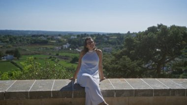 Beyaz elbiseli genç İspanyol kadın locorotondo, puglia, İtalya 'da güneşli bir günün tadını çıkarıyor. Etrafı yemyeşil manzaralar ve tarihi cazibeyle çevrili..