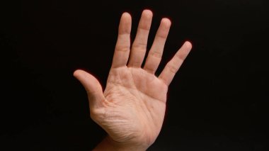 Siyah arka planda avuç içi açık bir erkek eli, derinin detaylı çizgilerini ve dokusunu gösterir.