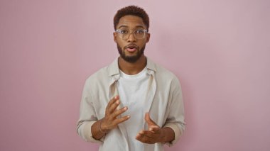Gözlüklü yakışıklı Afro-Amerikan genç adam pembe arka planda duruyor.