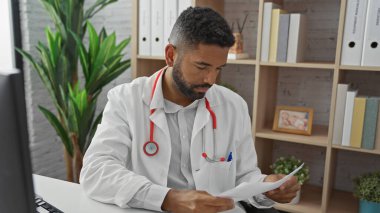 Laboratuvar önlüğü giyen, sakallı, odaklanmış genç, yetişkin bir zenci, klinikteki evrakları gözden geçiriyor..