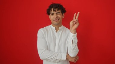 Kırmızı arka planda izole edilmiş, göz kırpan ve işaret eden İspanyol genç adam..