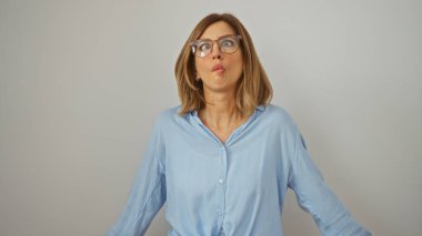 Gözlüklü, mavi gömlekli, izole beyaz arka planda komik bir yüz ifadesi takınan bir kadın.