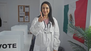 Steteskoplu gülümseyen genç bir kadın Meksika 'da bir üniversite odasında bayraklı kameraya bakıyor..