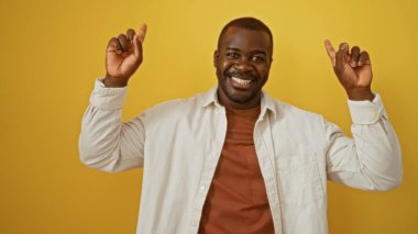 Gülümseyen ve yukarı bakan genç adam, parlak sarı bir arka plana izole edilmiş.