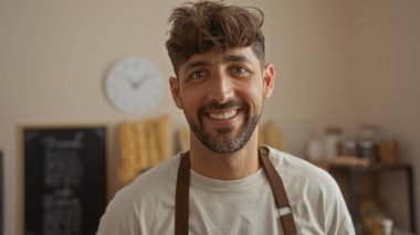 Fırın odasında gülümseyen genç bir adam, arka planda ekmek ile kapalı bir ortamda mutlu ve çekici bir erkek gösteriyor..