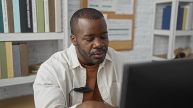 Ofiste çalışan yakışıklı genç bir adam, bir bilgisayar ekranına odaklanmış, raflarla çevrili, duvarında kitaplar ve evraklar var.