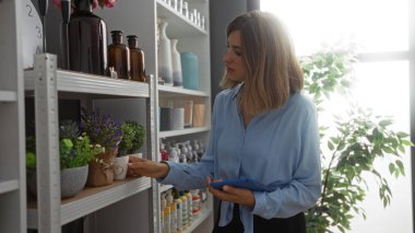Kadın elinde tablet tutarken saksı seçerek ev dekorasyonu mağazasından alışveriş yapıyor.