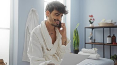 İspanyol asıllı genç bir adam spa salonunda telefonla konuşurken bir belge okuyor, rahat ve sağlıklı bir ortam ve şık bir iç tasarım sergiliyor..