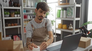 Ev dekorasyonu mağazasında çalışan, çeşitli dekorasyon malzemeleriyle çevrili, sakallı yakışıklı İspanyol bir adam.