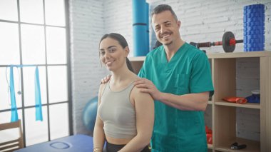 Bir kadın hasta ve erkek fizyoterapist kapalı bir fizik tedavi kliniğinde birlikte gülümsüyor..