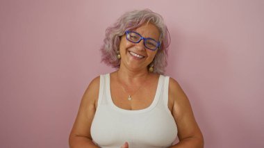 Gri saçlı ve gözlüklü olgun İspanyol kadın izole edilmiş pembe bir arka planda gülümsüyor.